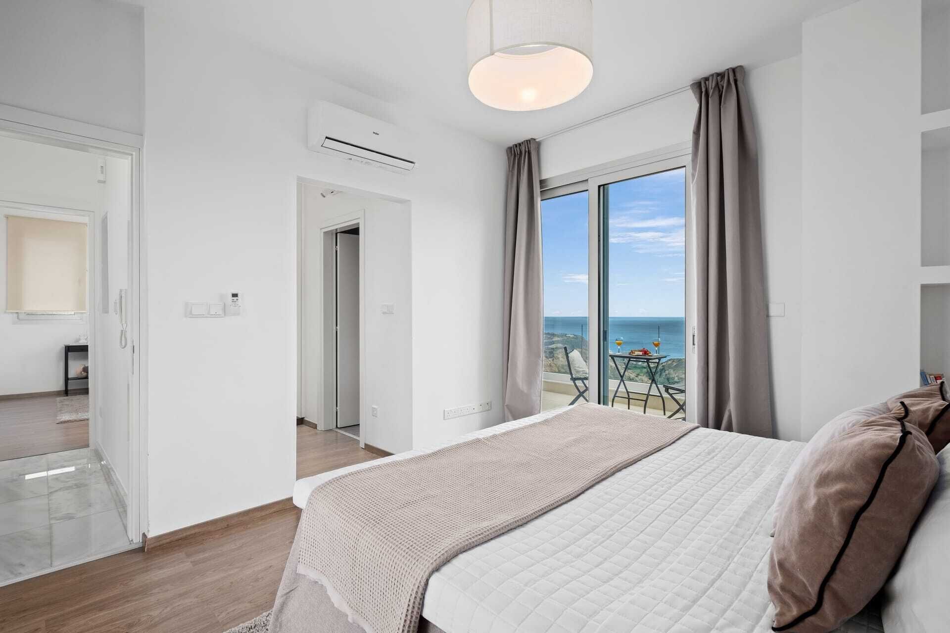 A modern hotel room with a large bed, a balcony with a view of the sea, and an air conditioning unit on the wall.