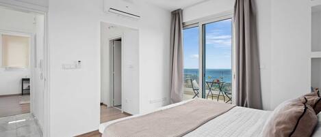 A modern hotel room with a large bed, a balcony with a view of the sea, and an air conditioning unit on the wall.