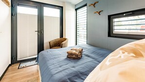 A bedroom with a bed, a chair, and a window. - Havel Houseboat Serenity (Zehdenick)