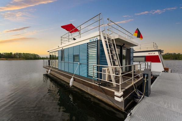 Een stilgelegen woonboot met een blauw uiterlijk, een overdekt dek en een wimpelstok met vlaggen.