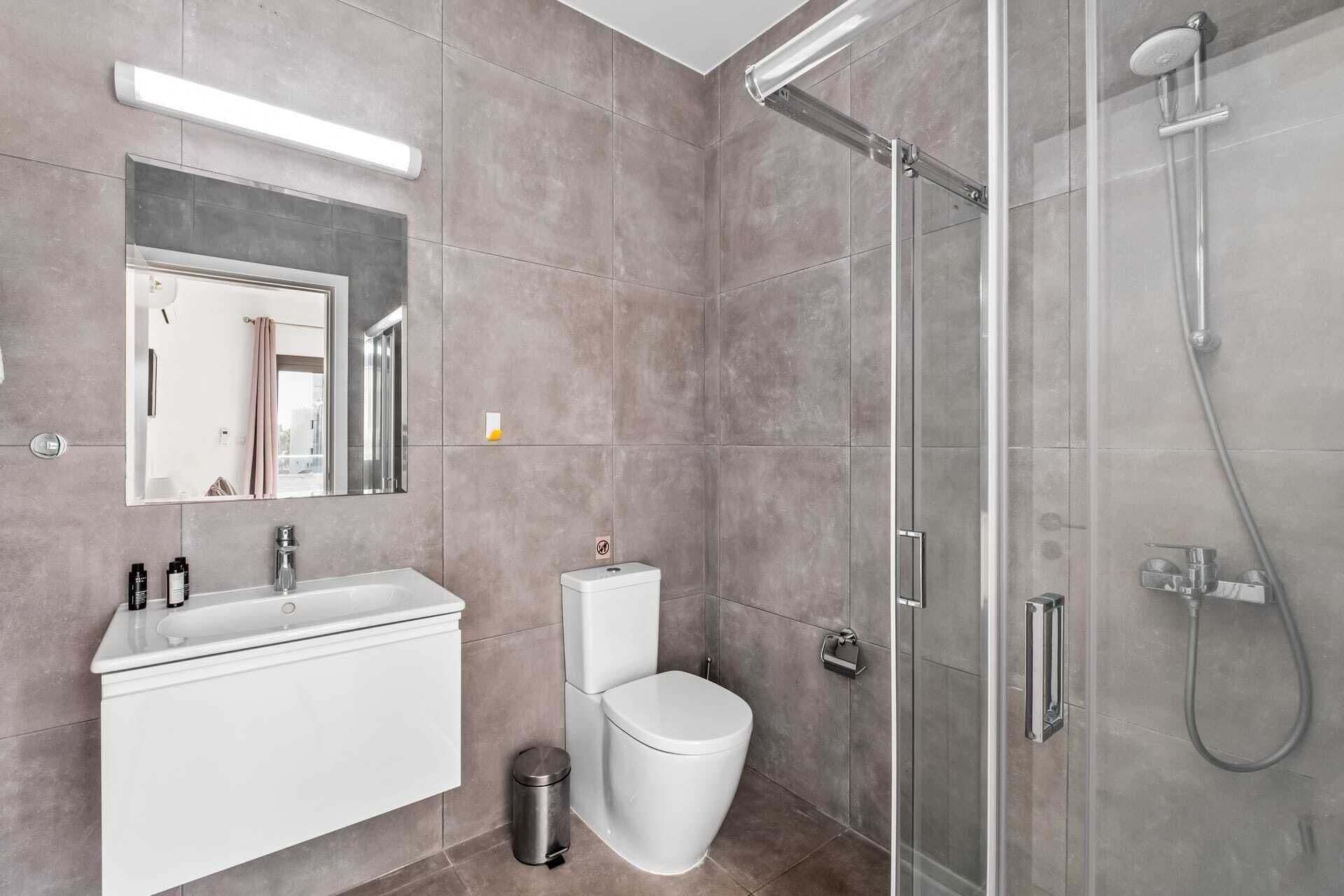 Un baño moderno con cabina de ducha de vidrio, lavamanos blanco y un inodoro.
