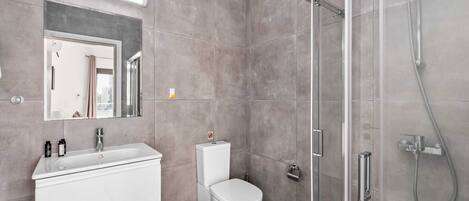 Un baño moderno con cabina de ducha de vidrio, lavamanos blanco y un inodoro.
