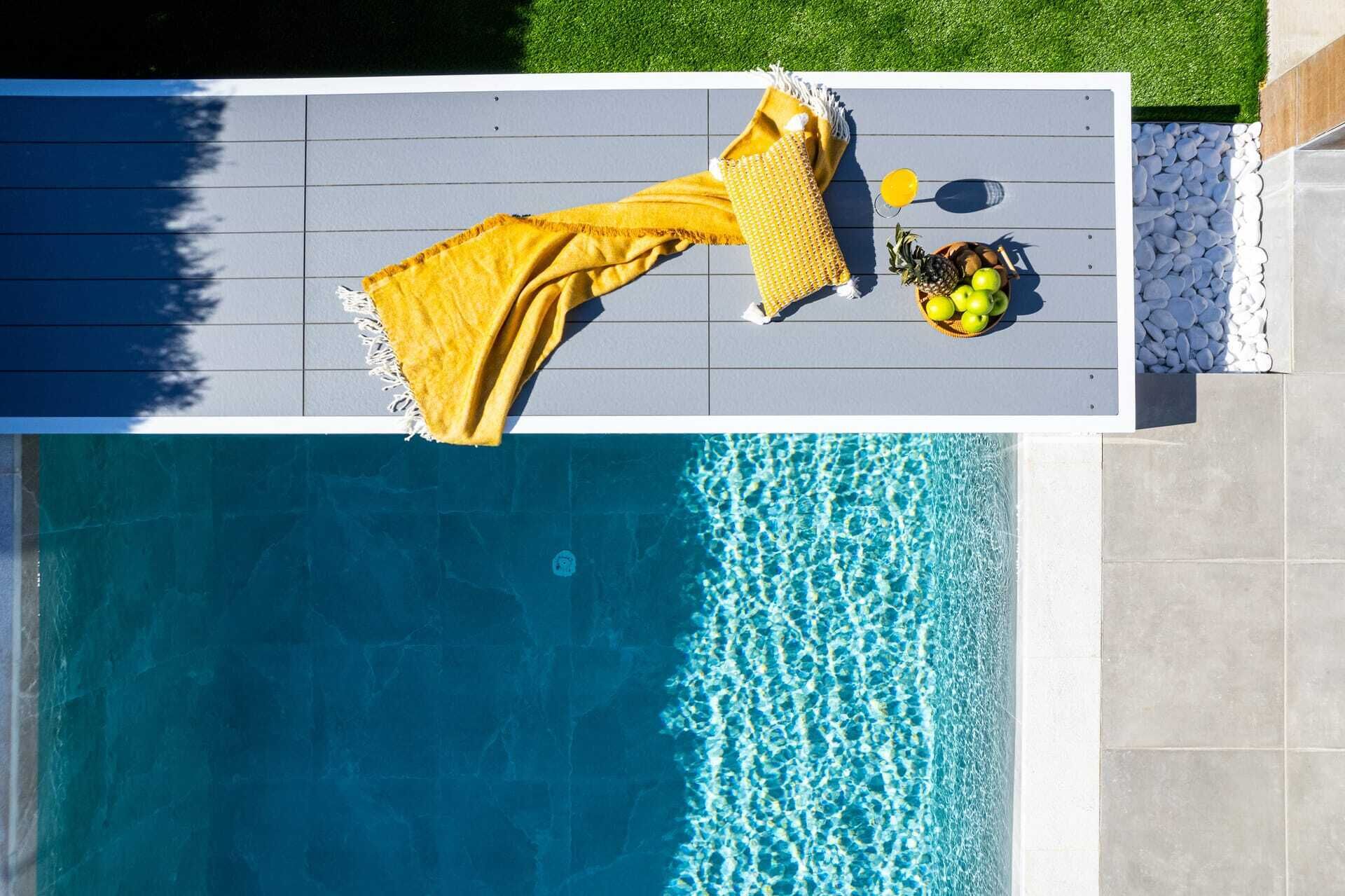 A poolside area with a yellow towel and a basket of fruit.