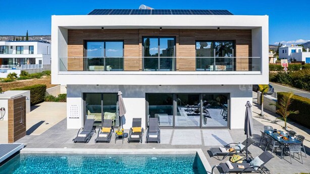 A modern two-story building with a swimming pool, lounge chairs, and a solar panel roof. - Soleil Luxury Villa by Nomads (Pegeia)
