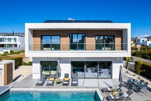 A modern two-story building with a swimming pool, lounge chairs, and a solar panel roof. - Soleil Luxury Villa by Nomads (Pegeia)