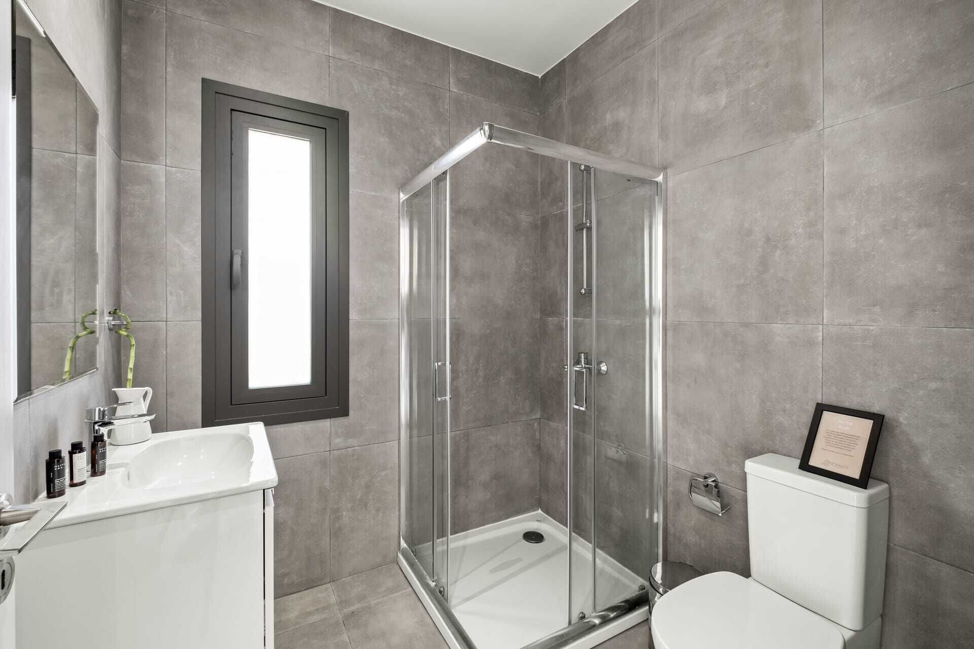 A modern bathroom with a glass shower enclosure, a white sink, and a toilet.