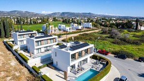 A modern residential building with solar panels, a swimming pool, and a view of a residential area with houses and greenery. - Soleil Luxury Villa by Nomads (Pegeia)
