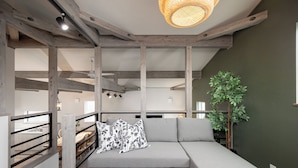 Una sala de estar moderna con un sofá seccional gris, una mesa de centro negra, vigas de madera y una lámpara colgante.