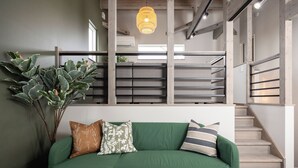 Un sofá verde con cojines estampados, una planta grande y una escalera con barandilla de madera.