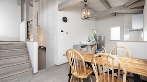 Una cocina moderna con suelo de madera, una mesa de comedor con sillas, una escalera y una lámpara colgante.