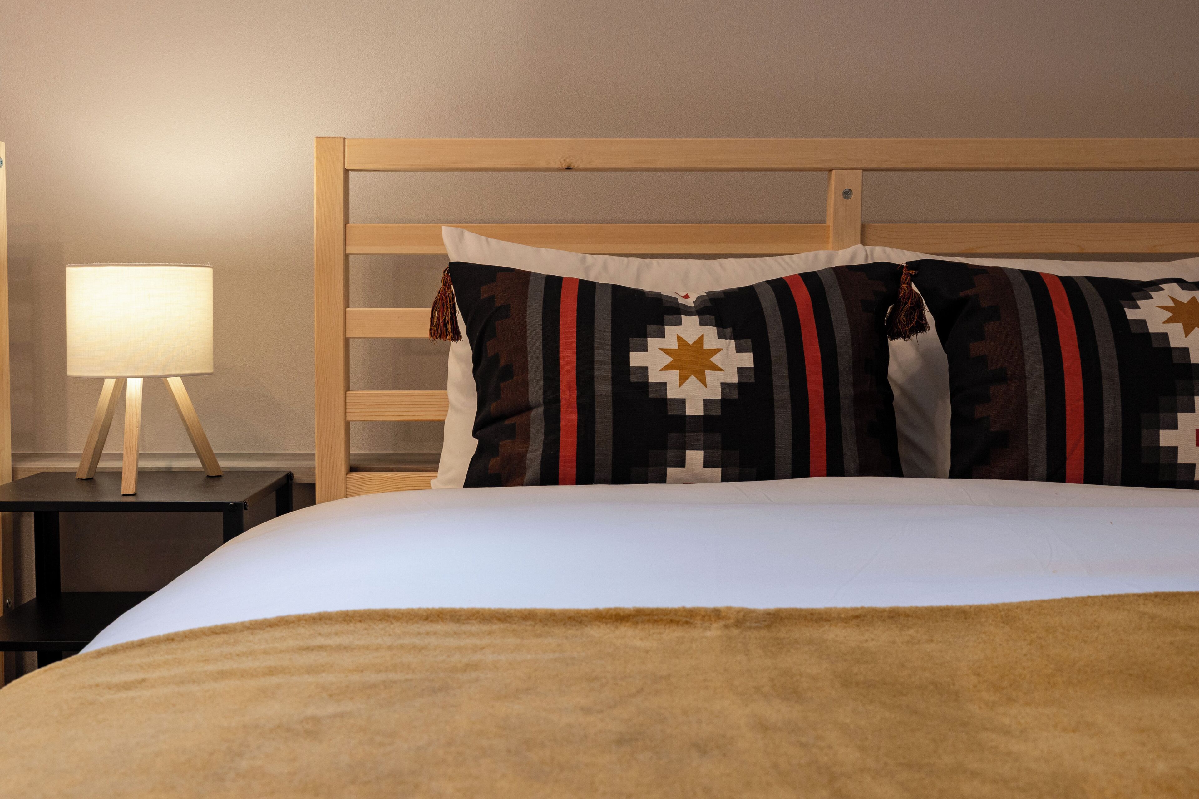Ein ordentlich gemachtes Bett mit weißer Decke und zwei dekorativen Kissen mit geometrischen Mustern.