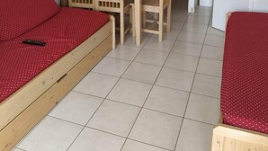 Une petite pièce propre et bien rangée, avec un lit, un bureau et une chaise. Une porte donne accès à une autre pièce.