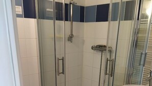 Une douche fermée par des parois de verre, avec un lavabo et un meuble de rangement blancs.