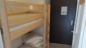 Une petite pièce, de taille modeste, avec un lit superposé, une porte sombre et un radiateur blanc.