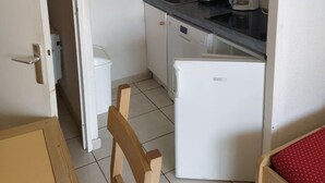 Une cuisine compacte avec des meubles blancs, un four à micro-ondes, une machine à café et un réfrigérateur.