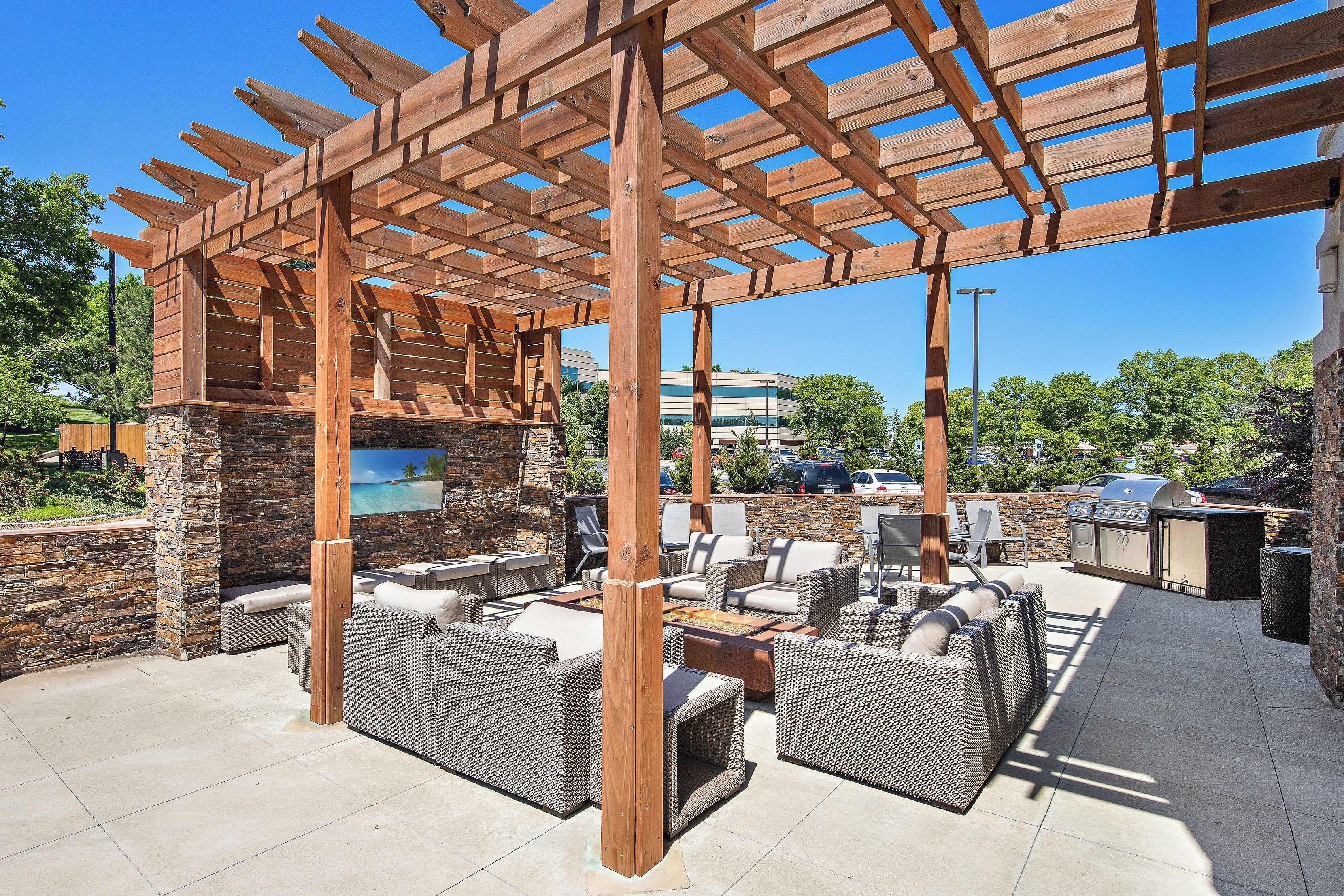Un patio exterior con pérgola de madera, paredes de piedra y mobiliario de exterior.