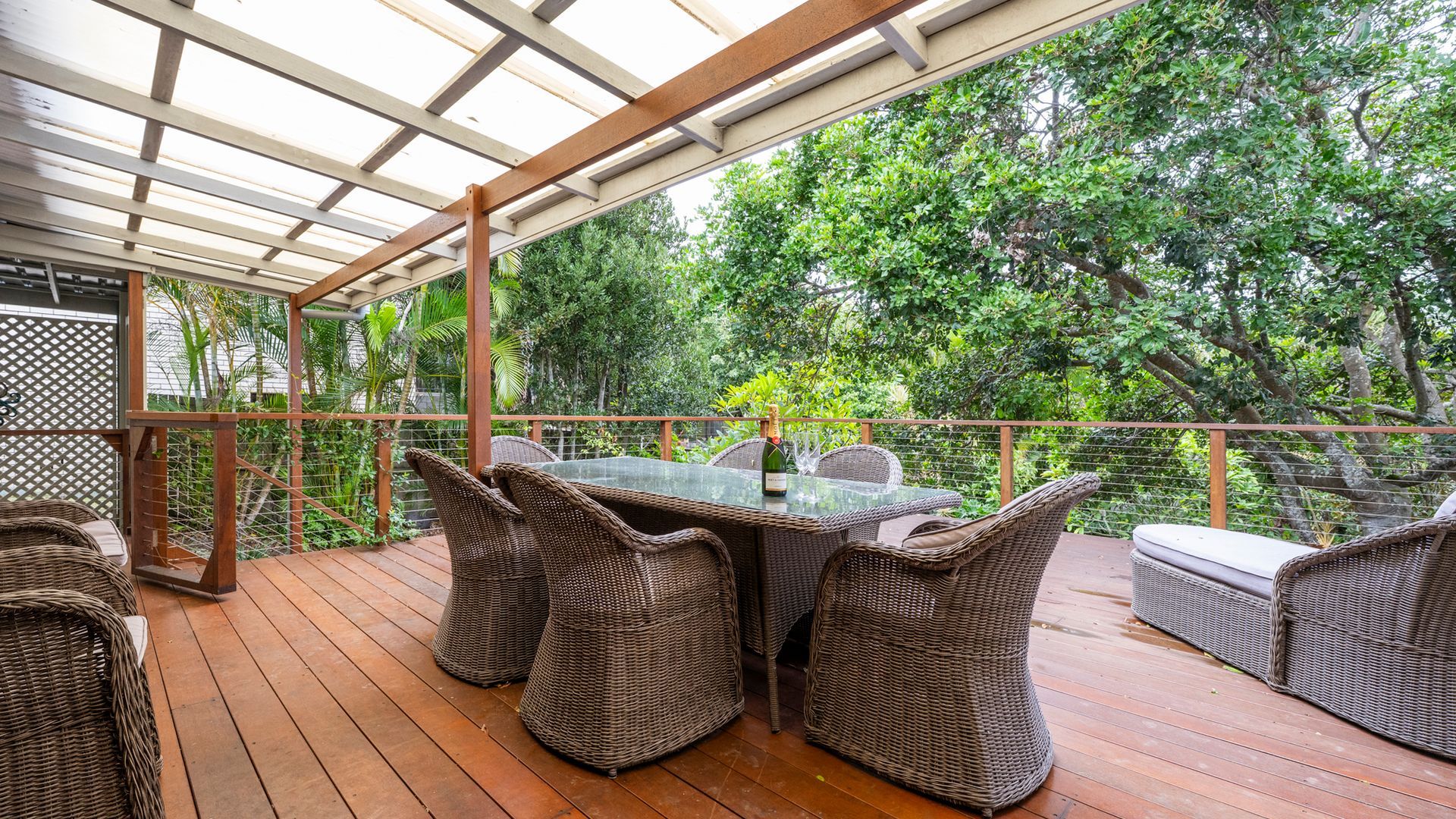Eine Terrasse im Freien mit Korbmöbeln, einem Glastisch und einer Champagnerflasche.