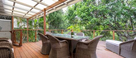 Eine Terrasse im Freien mit Korbmöbeln, einem Glastisch und einer Champagnerflasche.