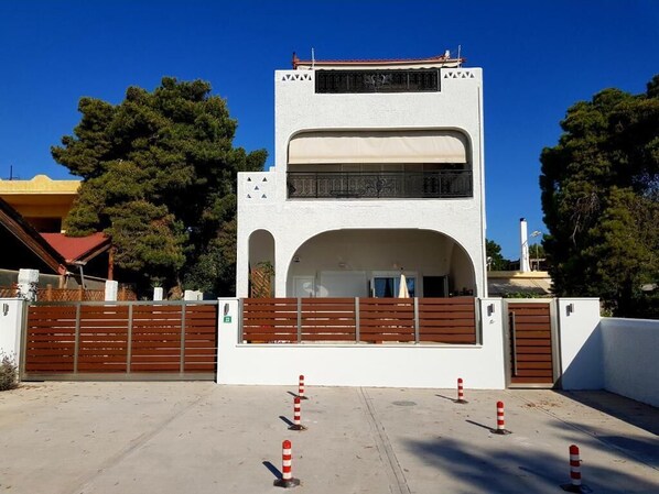 A modern building with a white facade, a central arched entrance, and a gated driveway. - Aphrodite's Apartments (Spata-Artemida)