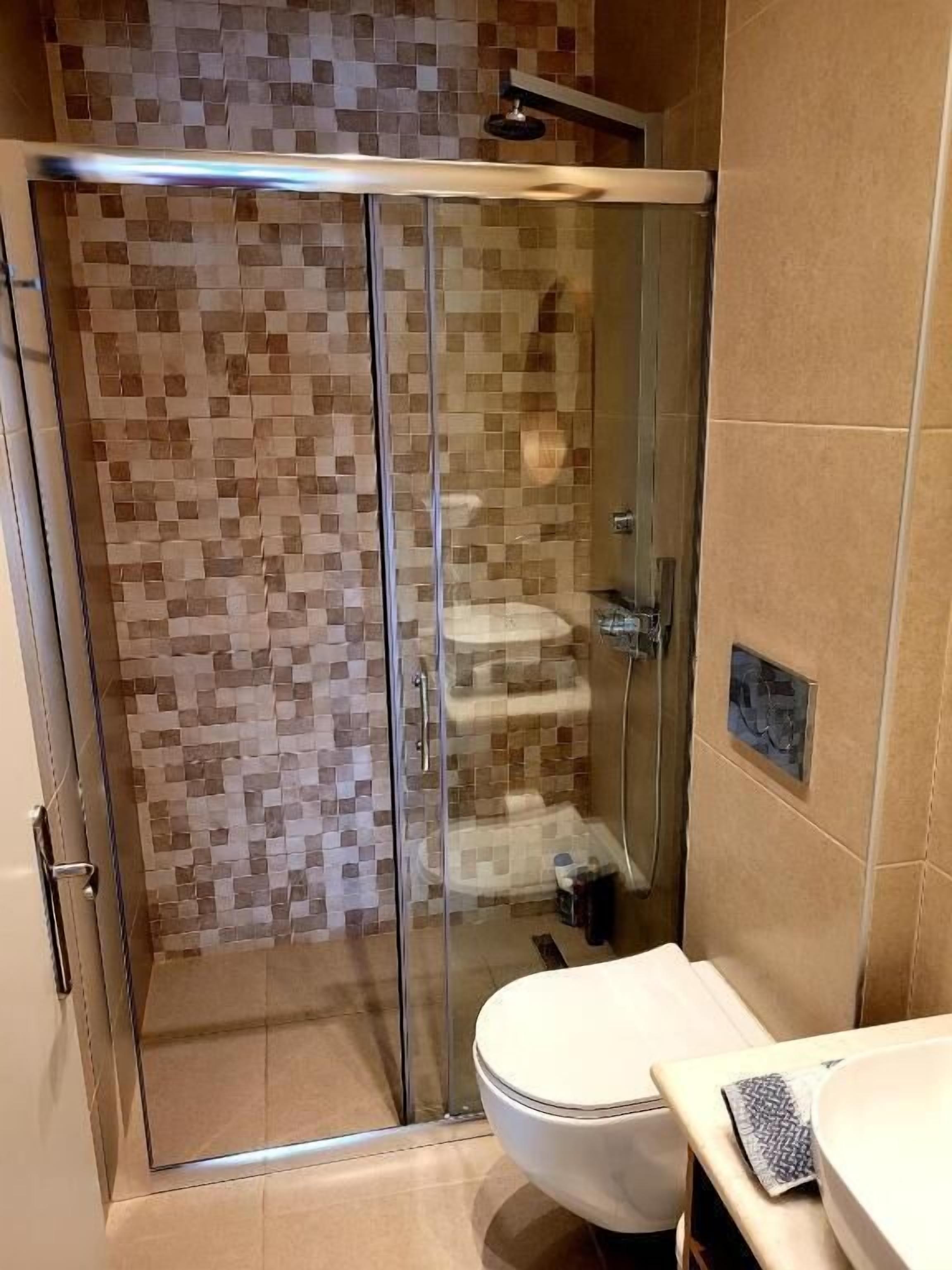 Une salle de bain avec une douche à parois de verre, des murs carrelés et des toilettes.