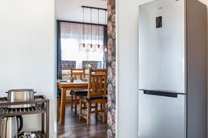 A kitchen with a stainless steel refrigerator, wooden dining table, chairs, and a kettle on a shelf. - Apartment 'Kleinert' with Shared Garden, Balcony and Wi-Fi (Blaufelden-Billingsbach)