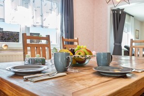 A dining table set with plates, cutlery, a bowl of fruit, and two cups.