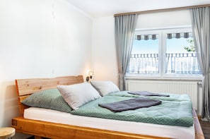 A bed with a wooden headboard, two pillows, a green patterned bedspread, and a dark blanket. - Apartment 'Kleinert' with Shared Garden, Balcony and Wi-Fi (Blaufelden-Billingsbach)