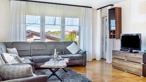 Een moderne woonkamer met een grijze bank, een salontafel, een tv-meubel en uitzicht op buiten.