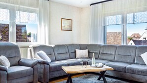Een moderne woonkamer met een grijze modulaire bank, een houten salontafel en uitzicht op gebouwen door grote ramen.