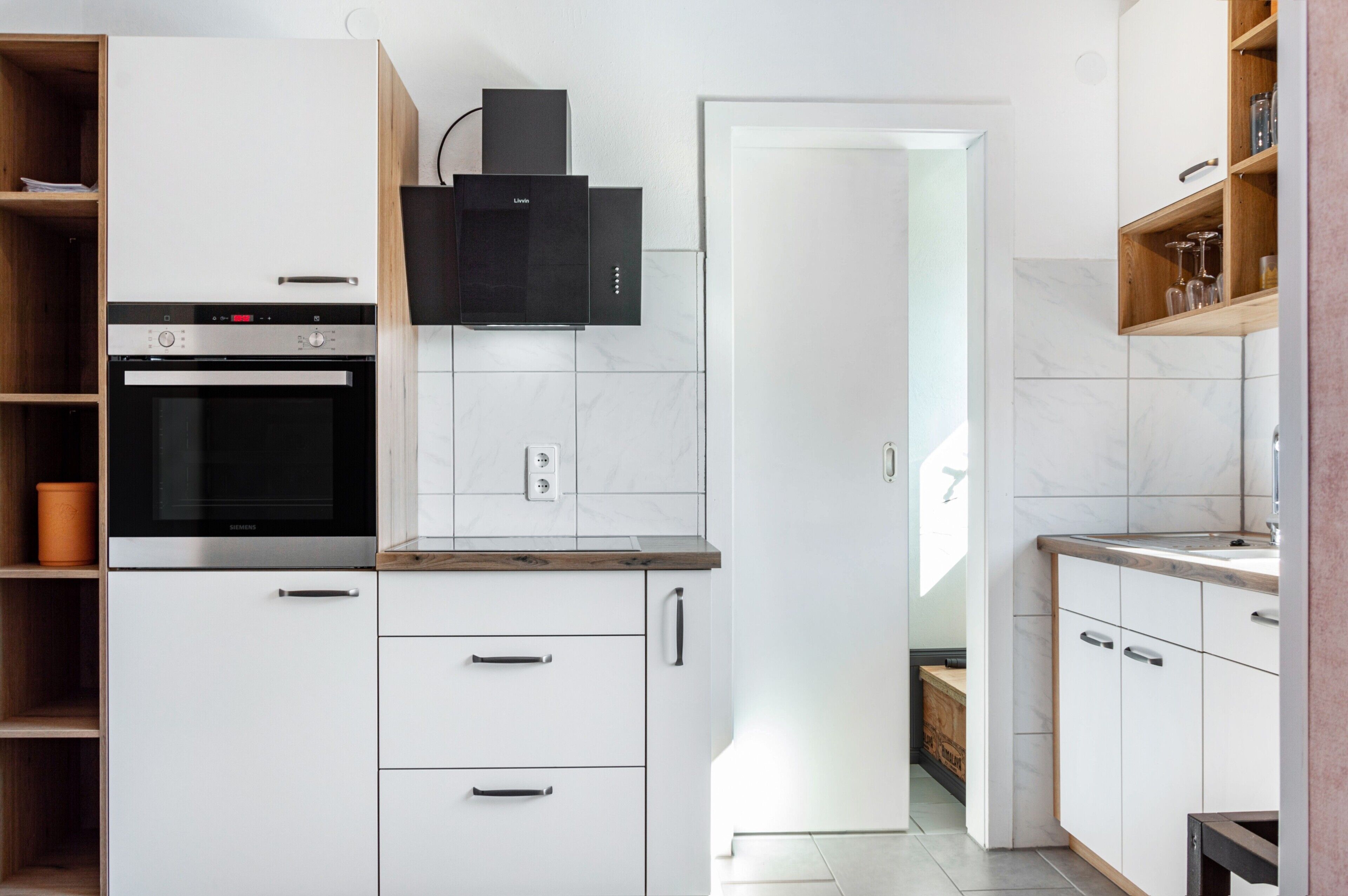 Une cuisine moderne avec des meubles blancs, un four encastré, une hotte aspirante et un plan de travail en bois.