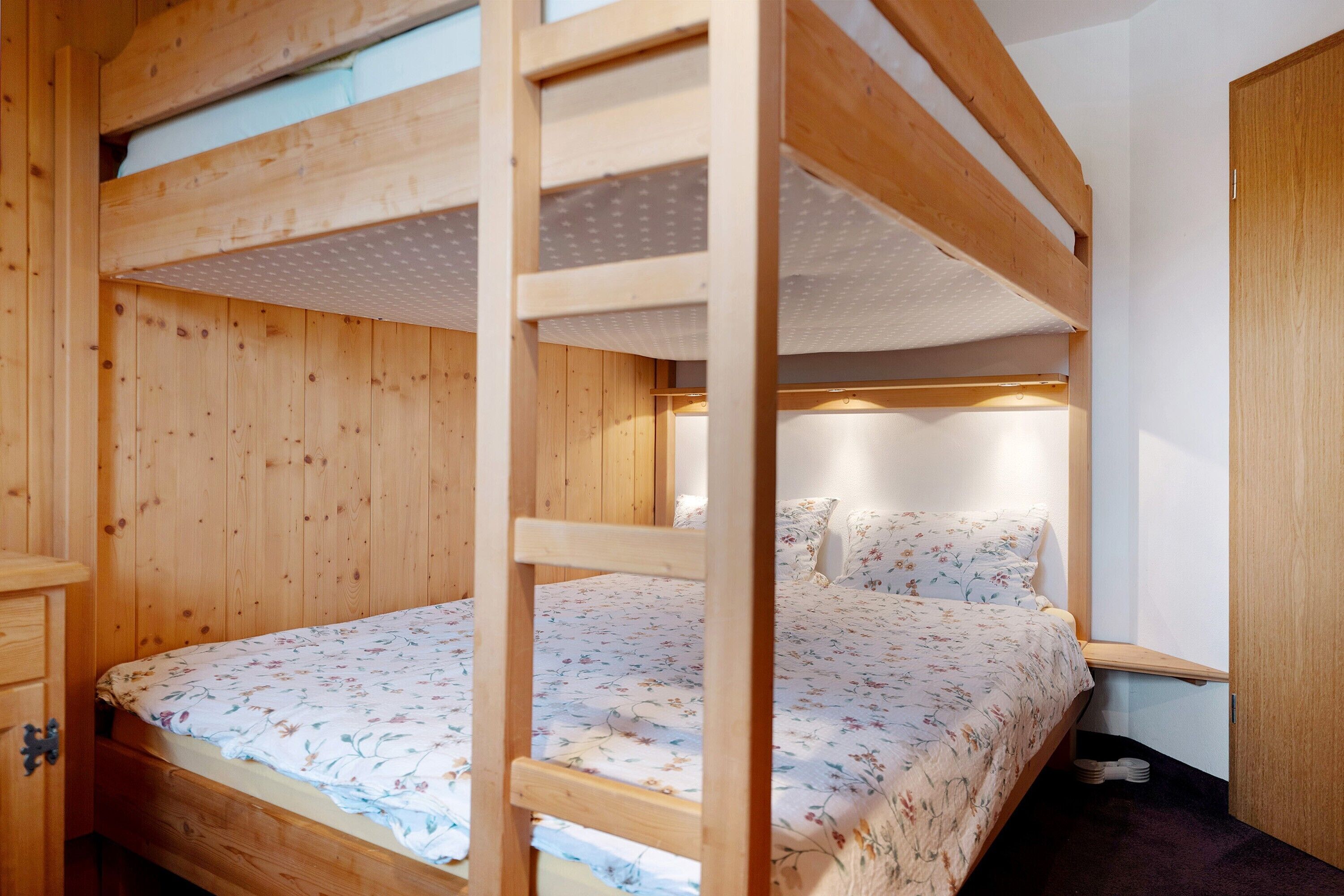 Een stapelbed met houten frame, een bloemenbedekking en een nachtkastje met lamp.