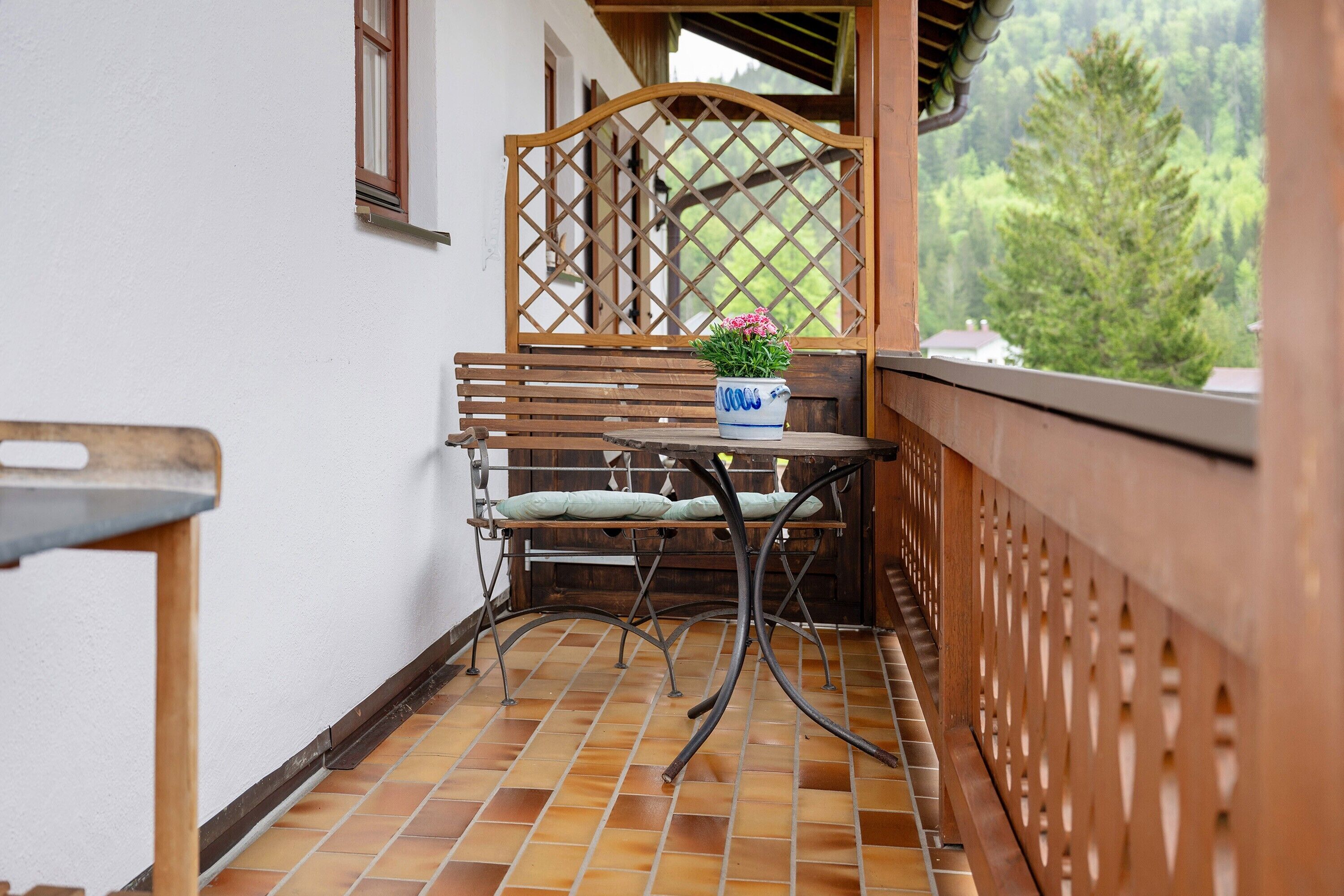 Un balcon avec une séparation en treillis de bois, une table en métal sur laquelle est posée une plante en pot et un banc.