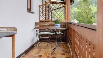 Un balcon avec une séparation en treillis de bois, une table en métal sur laquelle est posée une plante en pot et un banc.