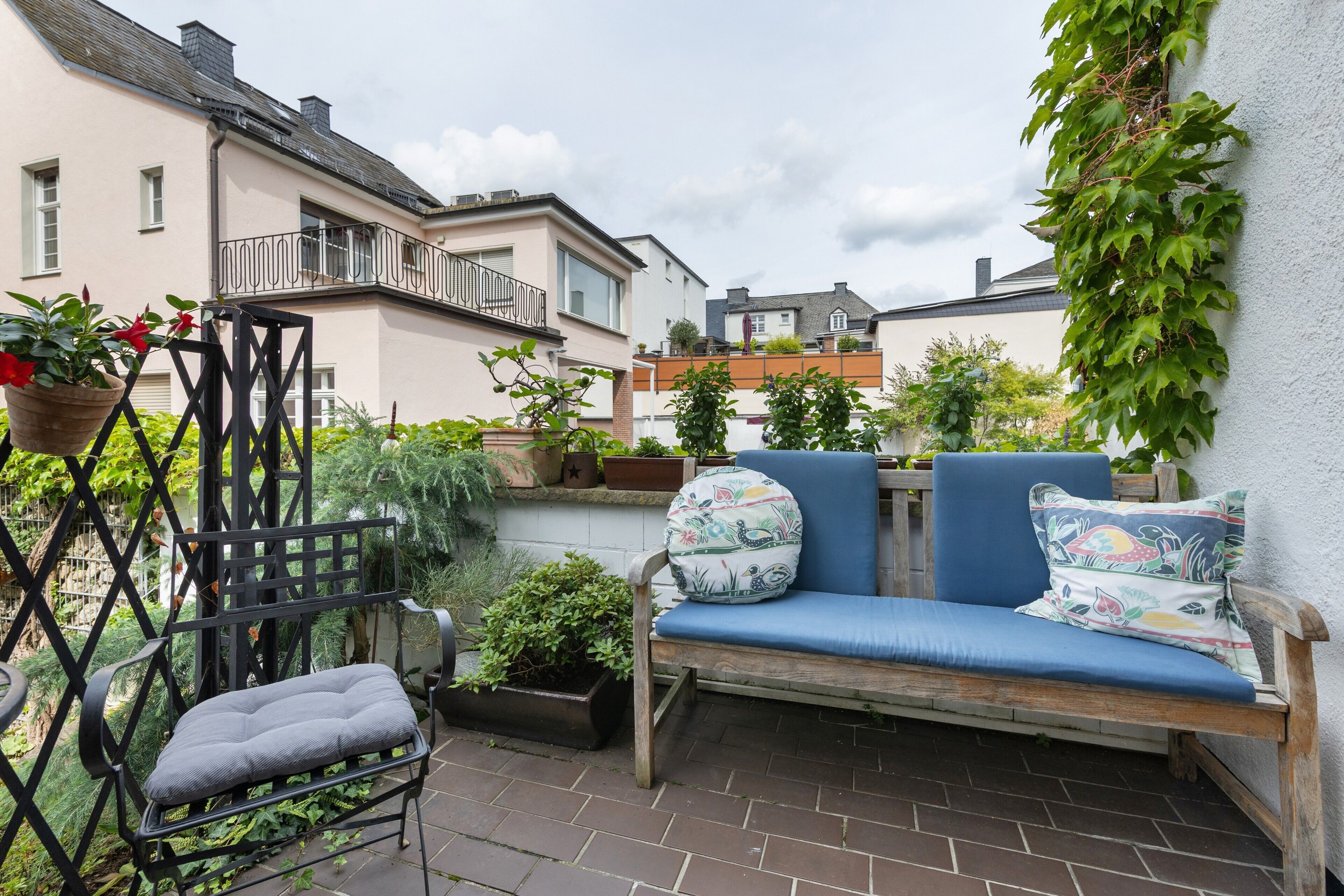 Une terrasse avec un canapé bleu, une chaise en métal et diverses plantes en pot.