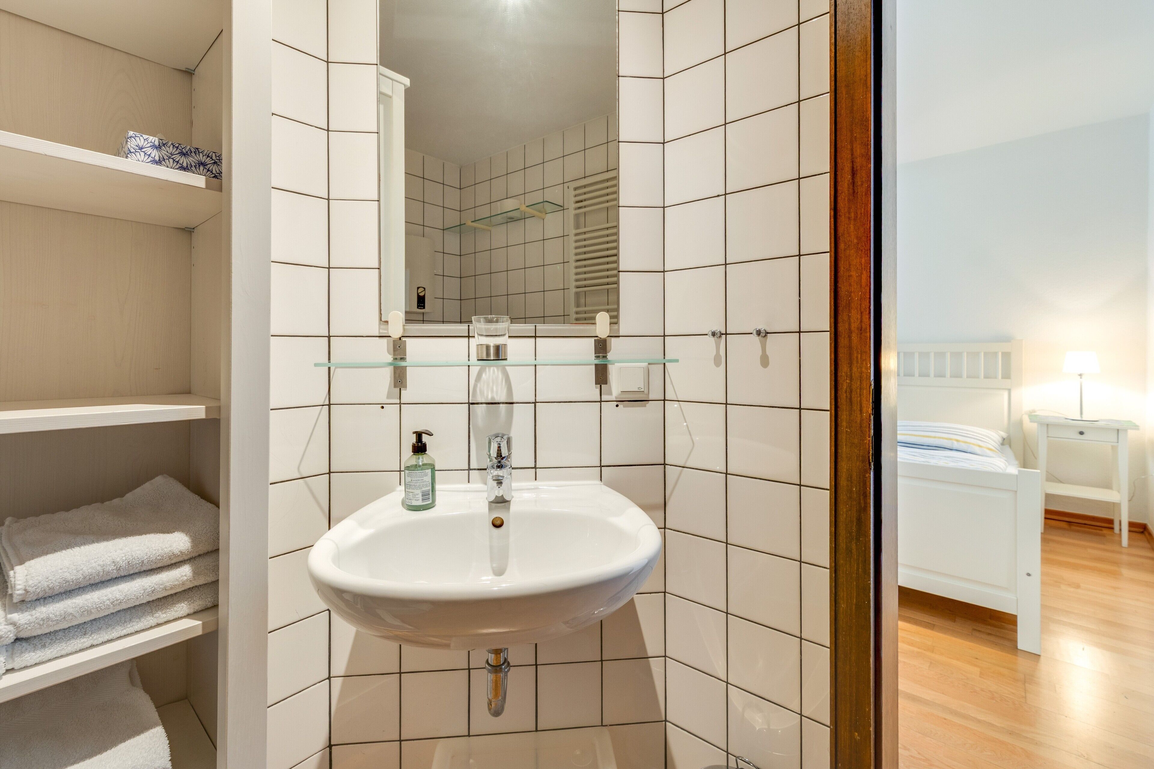 A bathroom with a white sink, a glass shelf, and a mirror.