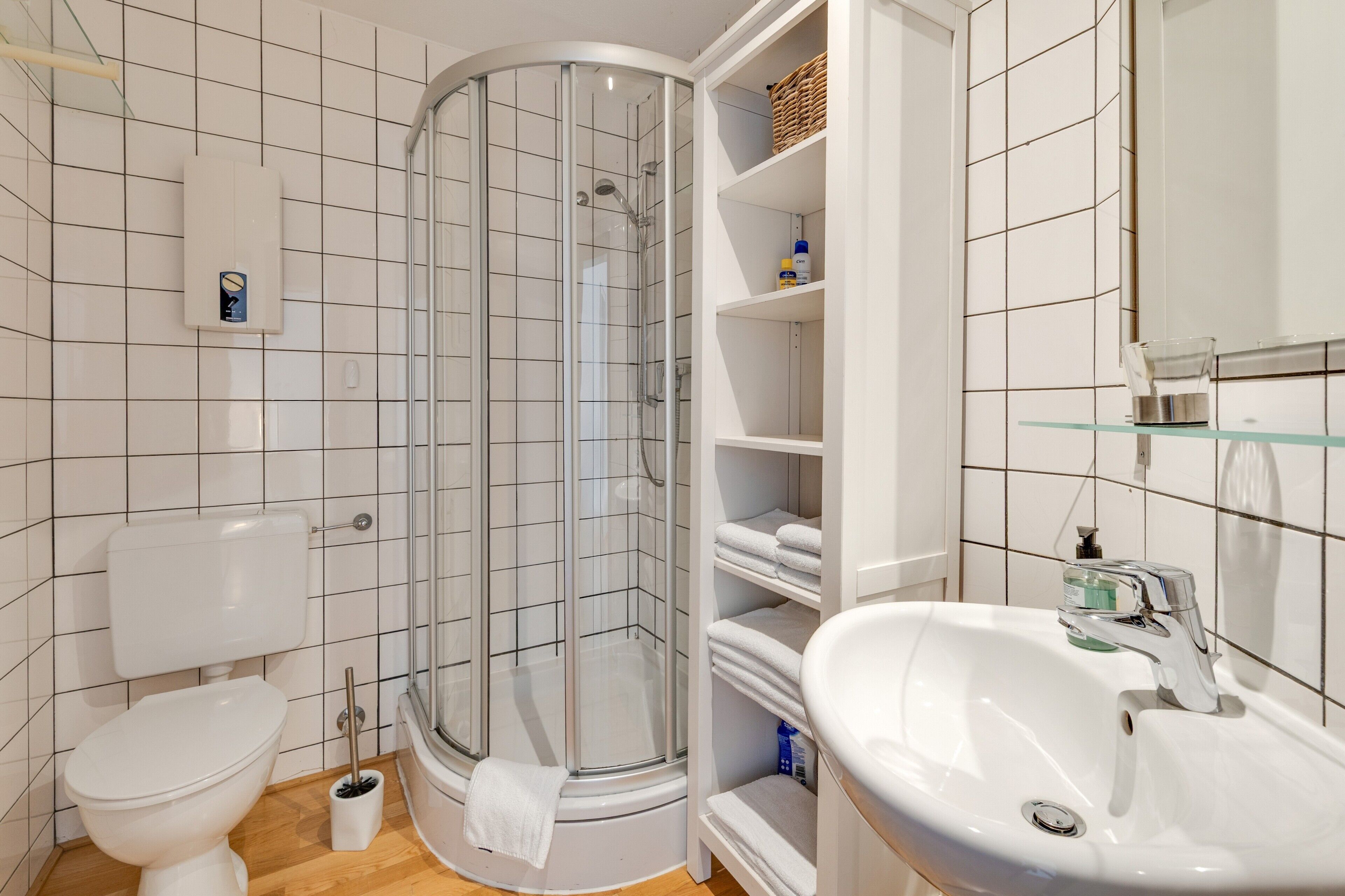 Ein Badezimmer mit einer Duschkabine, einer Toilette, einem Waschbecken und einem Ablagebereich mit Handtüchern.