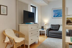 Un salon moderne avec un meuble blanc, un téléviseur à écran plat, un canapé gris, un fauteuil en osier et un tableau accroché au mur.