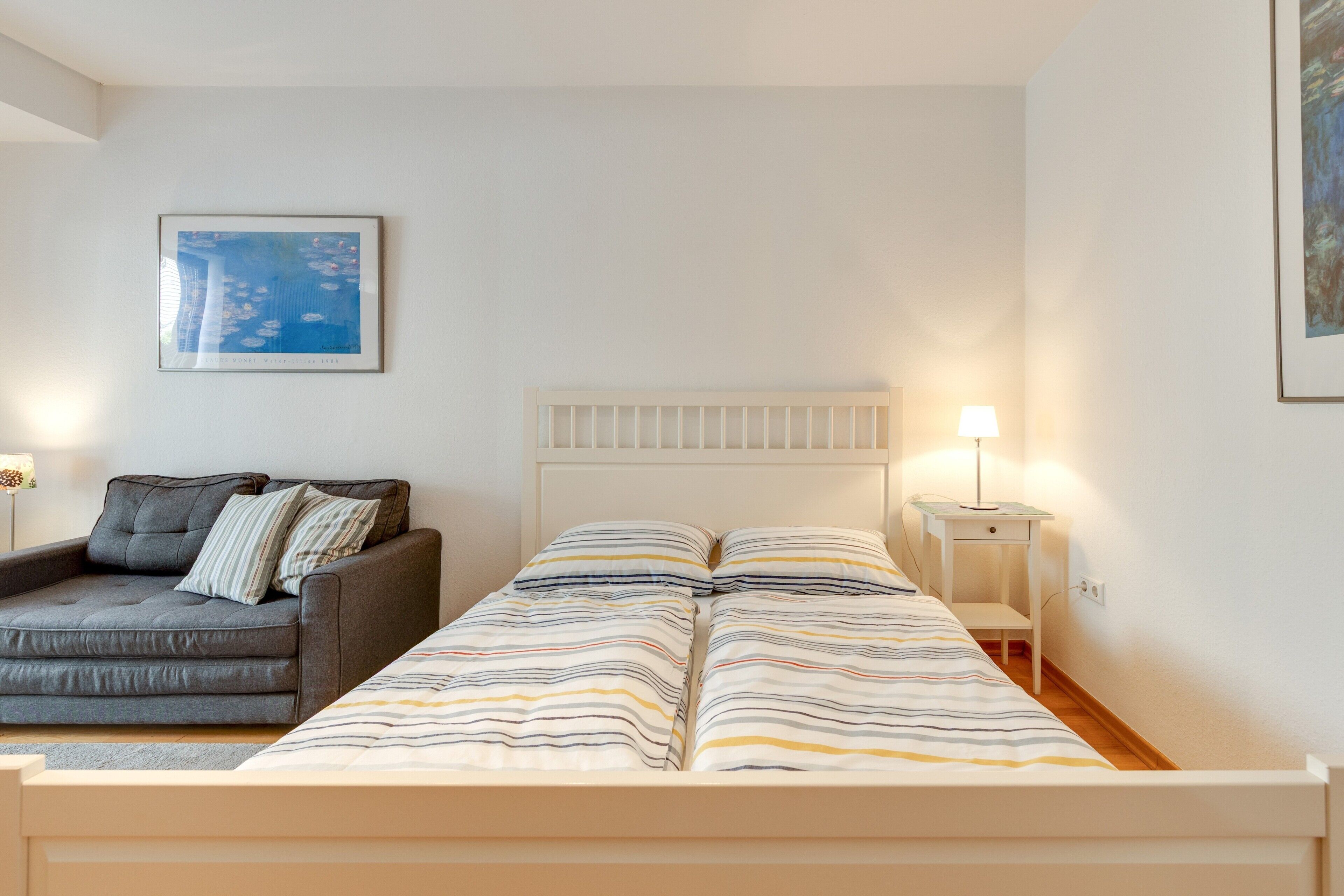 Ein Schlafzimmer mit Bett, Schlafsofa, Nachttisch, Lampe und einem Bild an der Wand.