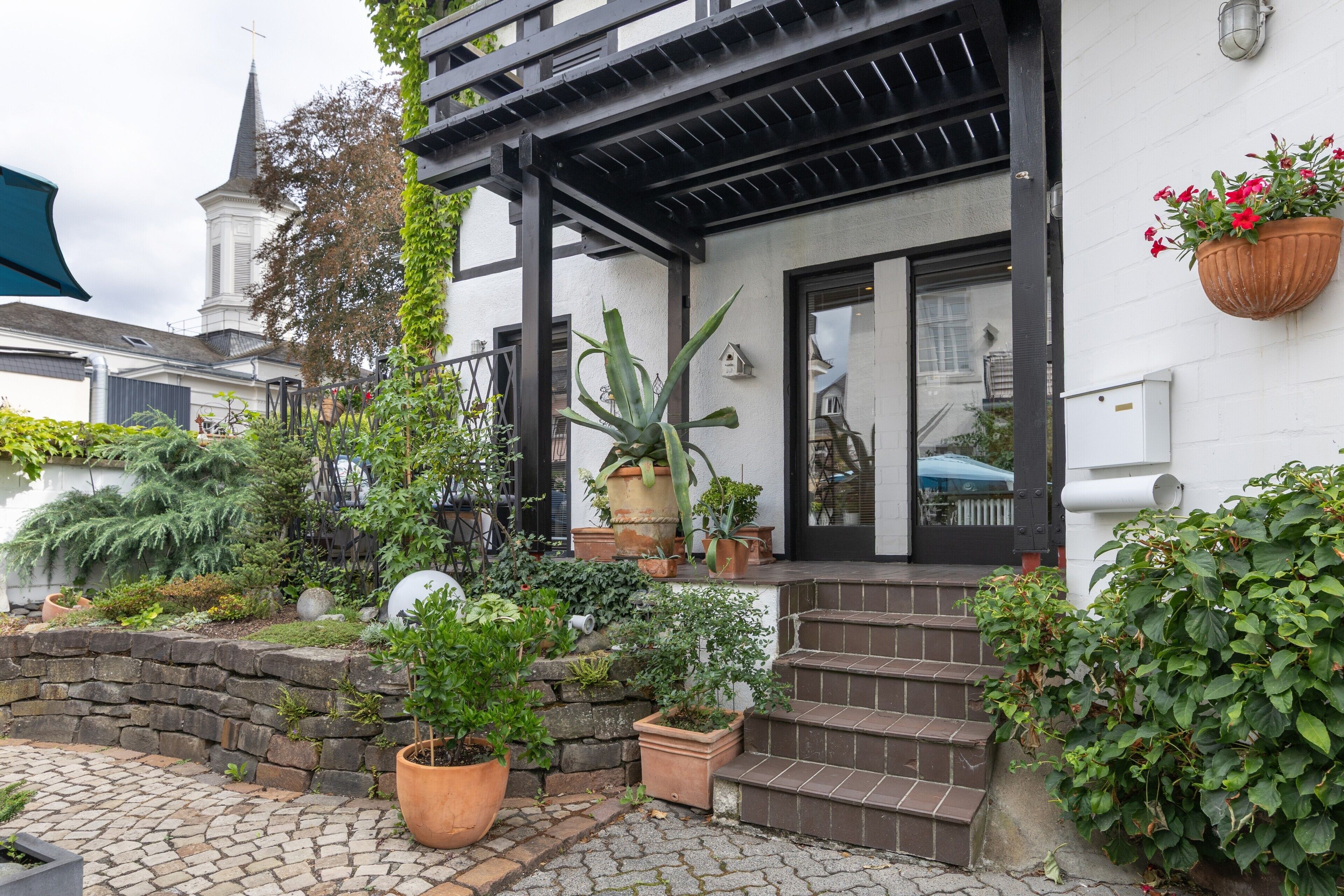 A house with a porch, potted plants, and a stone wall.