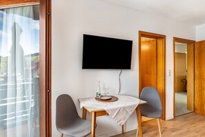 Una habitación con una mesa preparada para dos personas, un televisor montado en la pared y un ventanal corredero que da a un espacio exterior.