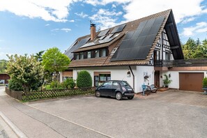 A traditional house with a sloped roof, solar panels, a parked car, and a fence.