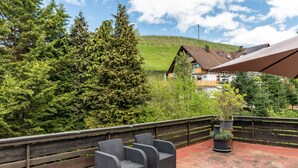 A terrace with wicker chairs, a wooden railing, and a view of a house with a sloped roof. - Room 'No. 5' with Shared Garden and Wi-Fi (Sasbachwalden)