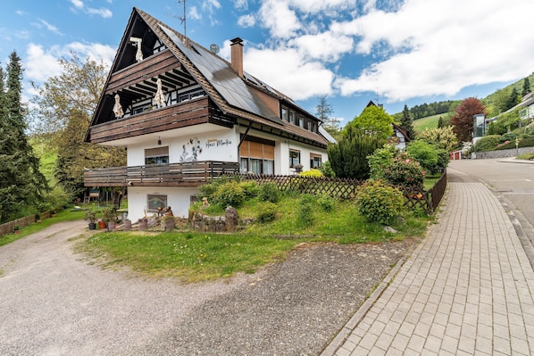A traditional chalet-style building with a sloped roof, a balcony, and a gravel driveway.