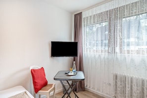 A room with a bed, a small table with a bottle, a remote control, and a TV mounted on the wall.
