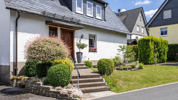 A house with a front door, steps leading to the entrance, a small porch, and a well-maintained garden with bushes and flowers. - Apartment 'Annes Stübchen' with Balcony and Wi-Fi (Schmallenberg)