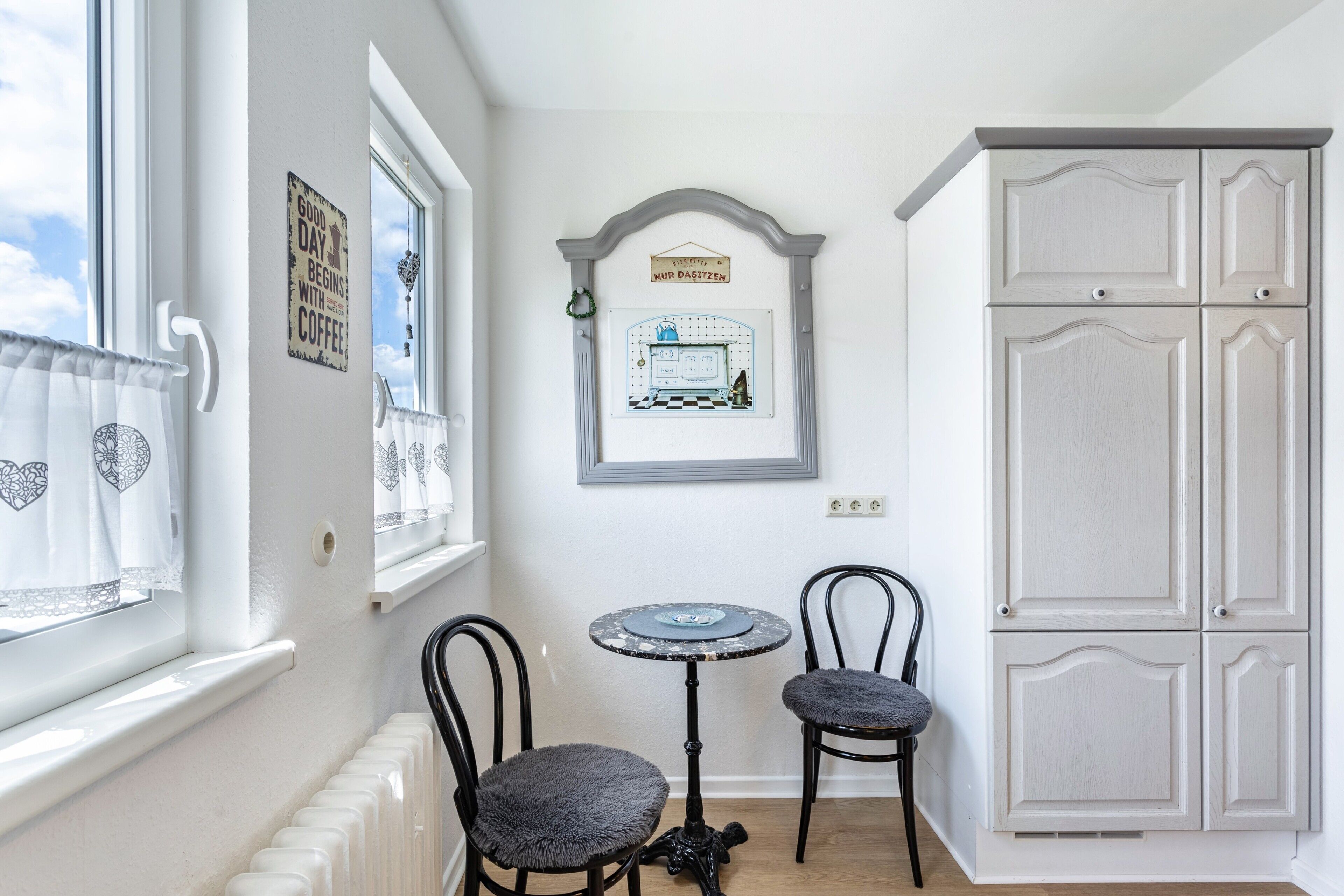 Une pièce avec un radiateur, deux chaises, une petite table et un meuble.
