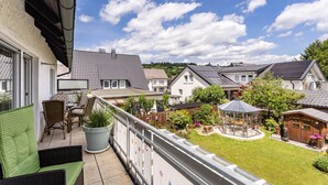 A balcony with wicker furniture, a potted plant, and a view of neighboring houses and a garden. - Apartment 'Annes St übchen' with Balcony and Wi-Fi (Schmallenberg)