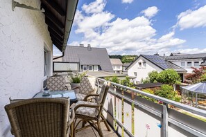 A balcony with wicker chairs and a table, overlooking a residential area with houses and a clear sky. - Apartment 'Annes Stübchen' with Balcony and Wi-Fi (Schmallenberg)