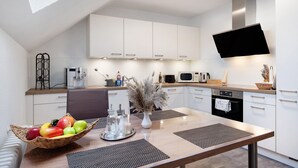 A modern kitchen with white cabinets, a flat-screen TV, a dining table with placemats, and a fruit bowl. - Apartment 'Kessler Waldblick' with Balcony and Wi-Fi (Häusern)
