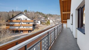 A balcony with a view of houses and wind turbines, a wooden railing, and a modern building facade. - Apartment 'Kessler Waldblick' with Balcony and Wi-Fi (Häusern)